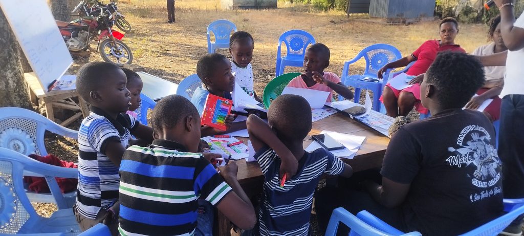 RICCA beneficiaries, children in joint session with parents an an open space in Rukanga Kirinyaga county. The founder is facilitating the learning after school session